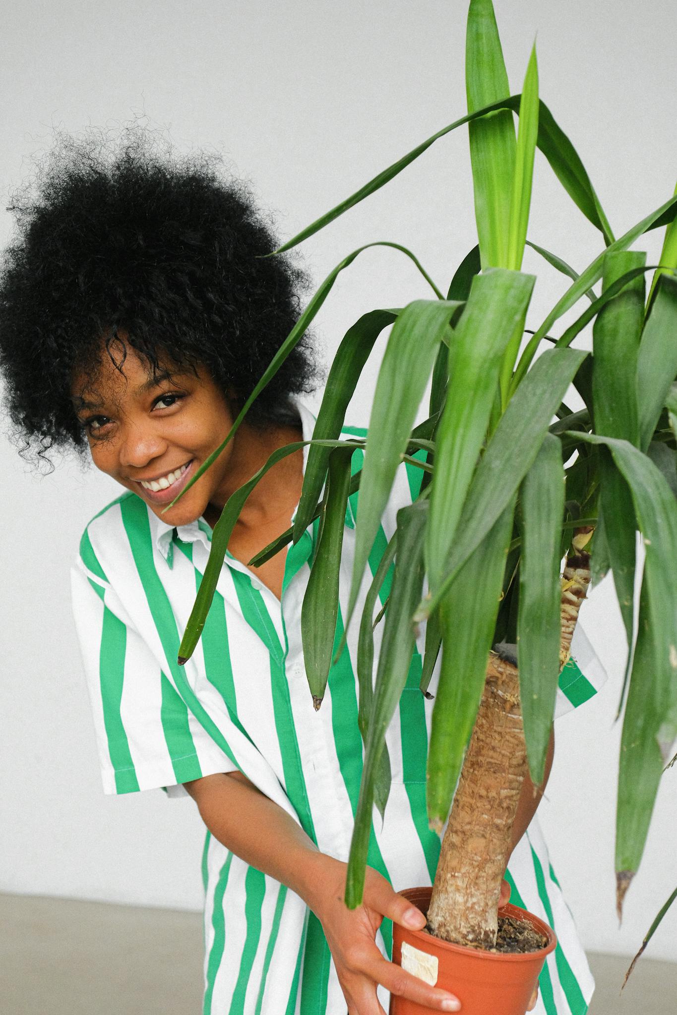 Cheerful woman holding a potted plant, expressing happiness in a casual striped shirt.